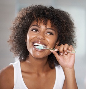 woman in white tank brushing teeth